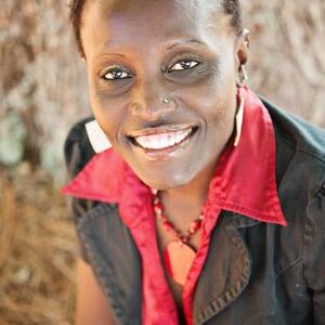 Dr. Ngumbi smiling in a red button up shirt with a black blazer jacket over it.