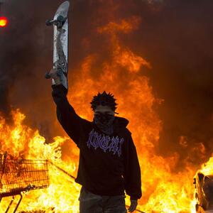 protester holding up skateboard in front of fires from the protests